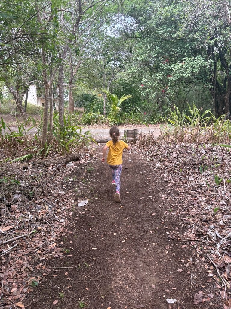 A girl in a yellow t-shirt running off down a leafy forest trail