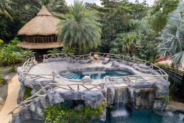 The thatched casita beside the hotel's natural rock-cut cave pool and waterfall, framed by jungle