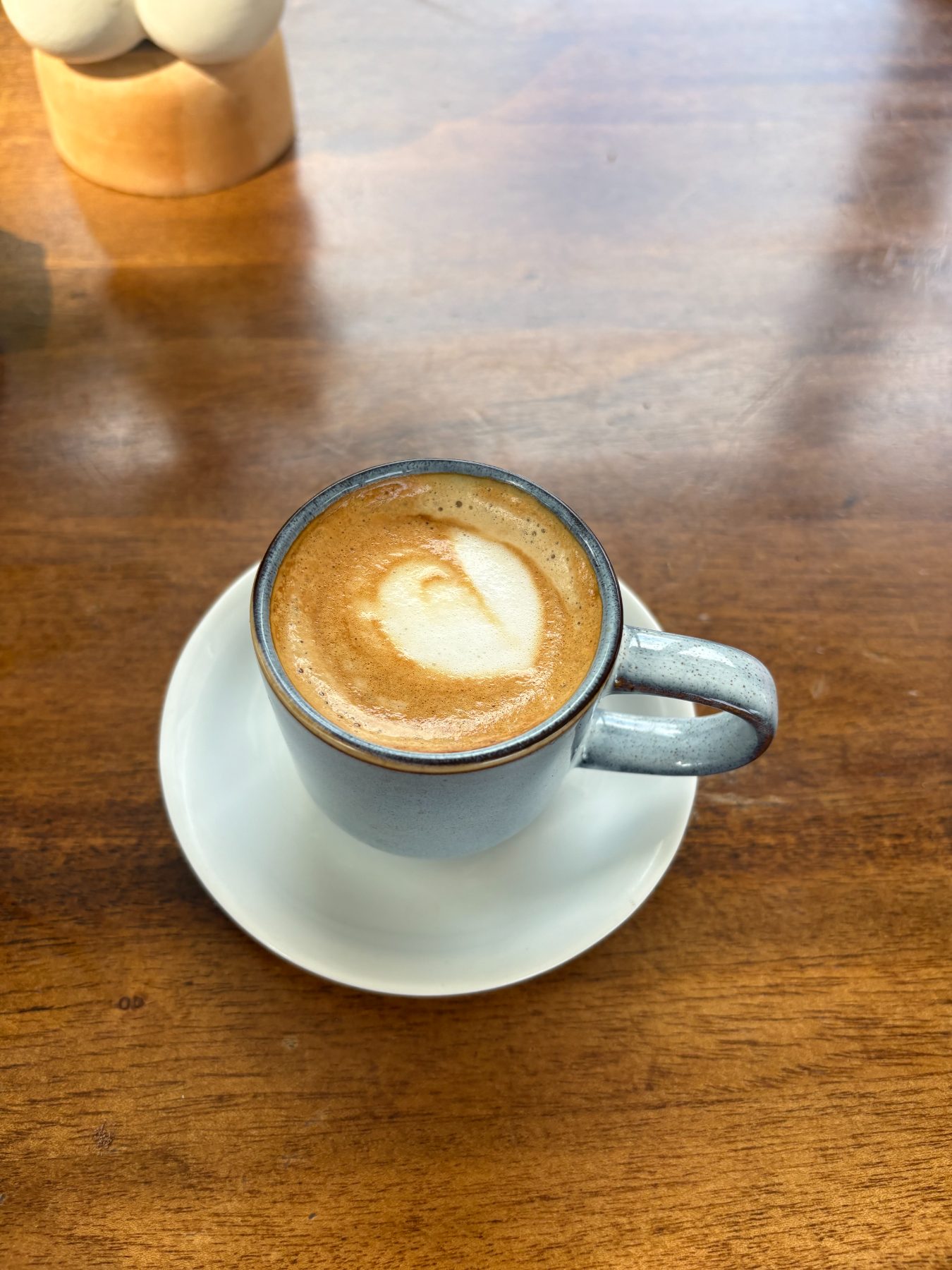 A freshly made flat white with latte art resting on a sunlit wooden table